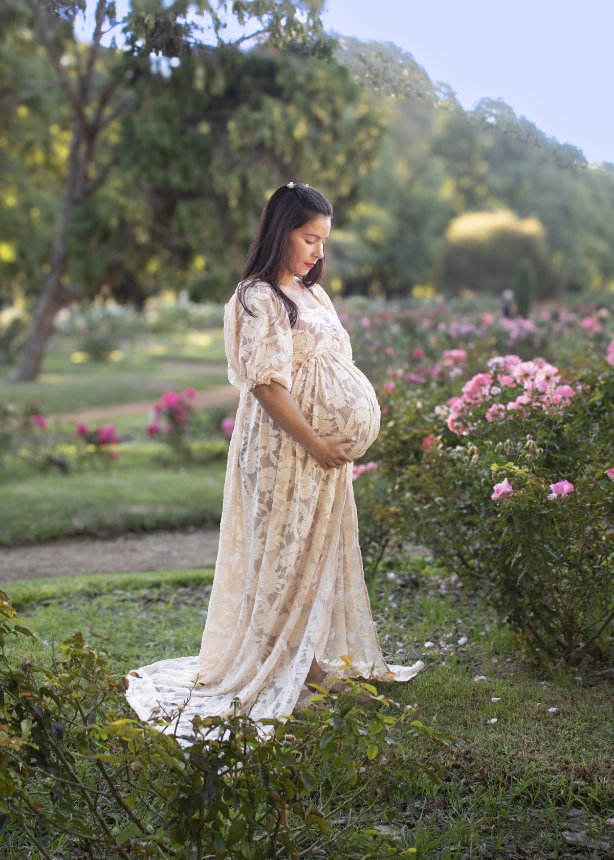 embarazada en jardín de rosas, de perfil mirando su panza, vestido romántico