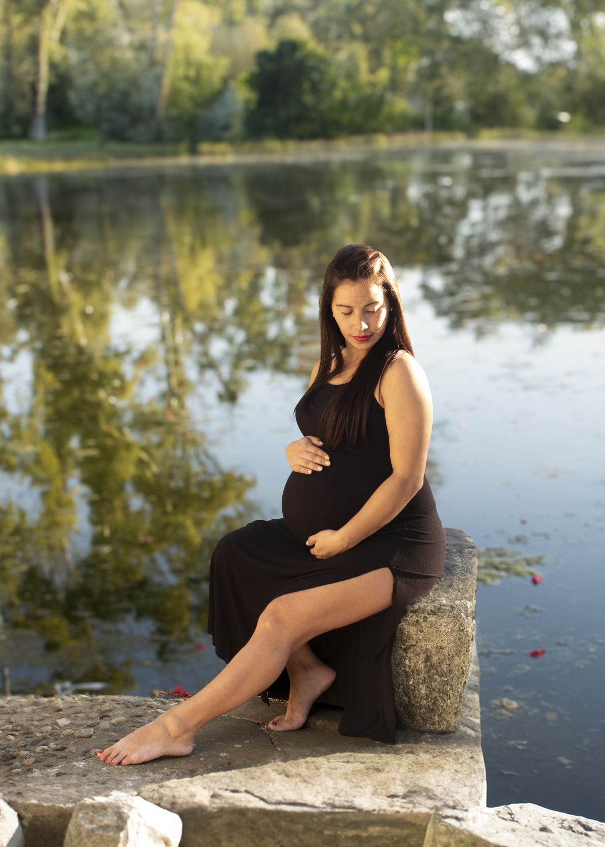 embarazada sentada sobre piedras de un lago, vestida de negro