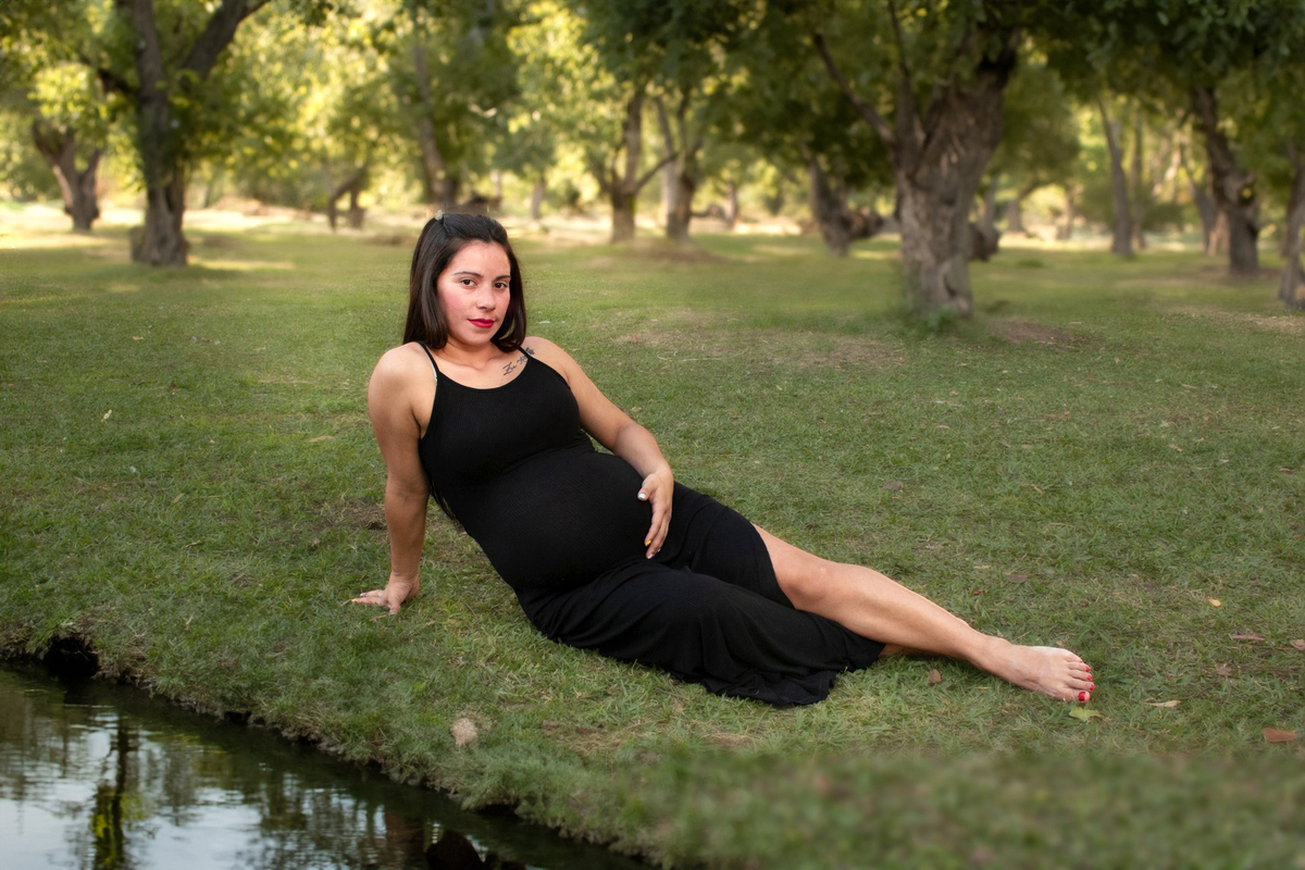 embarazada sentada sobre el césped a la orilla de un lago, vestida de negro vestida de negro