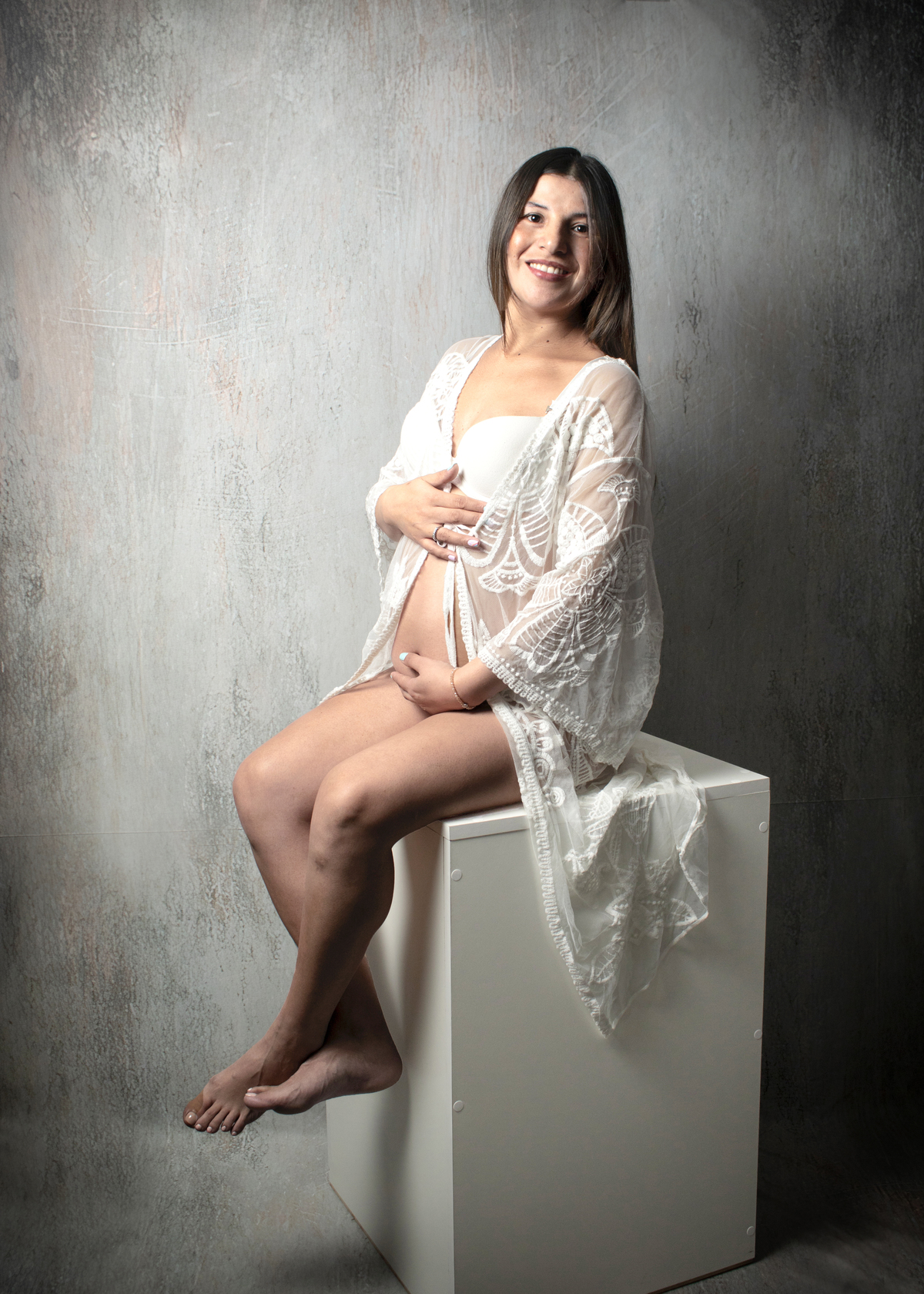 embarazada con bata calada blanca sentada sobre cubo blanco