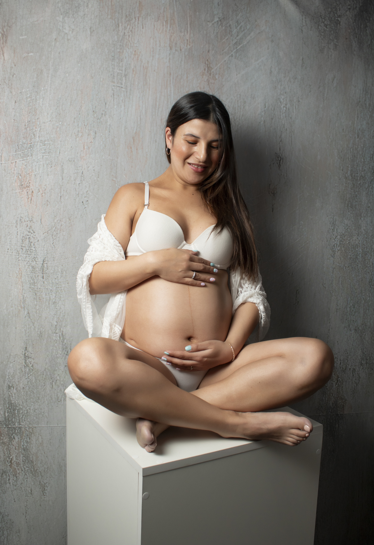 embarazada con ropa interior blanca y bata blanca sentada sobre un cubo blanco
