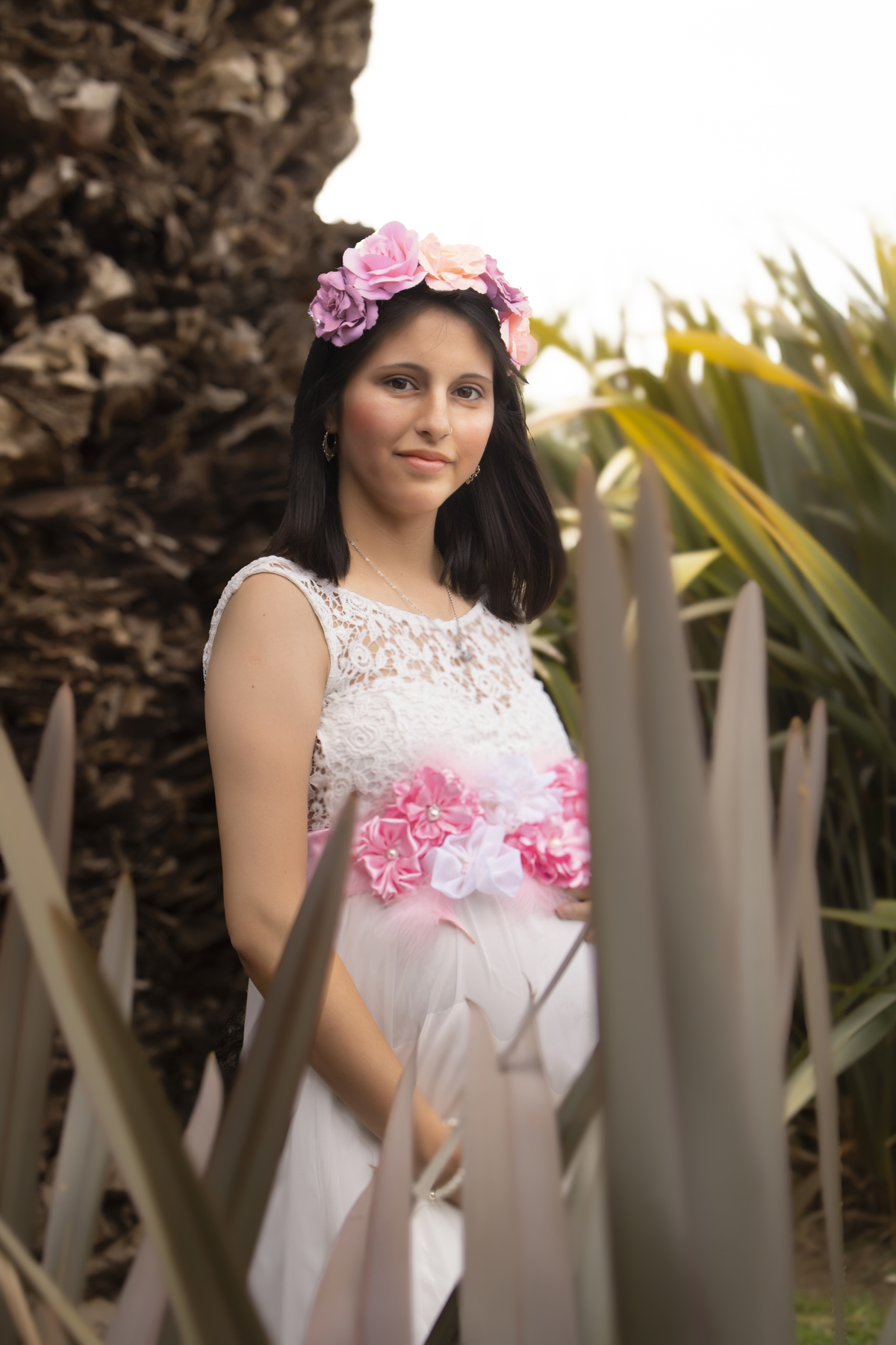 embarazada apoyada en tronco de palmera, fondo de plantas