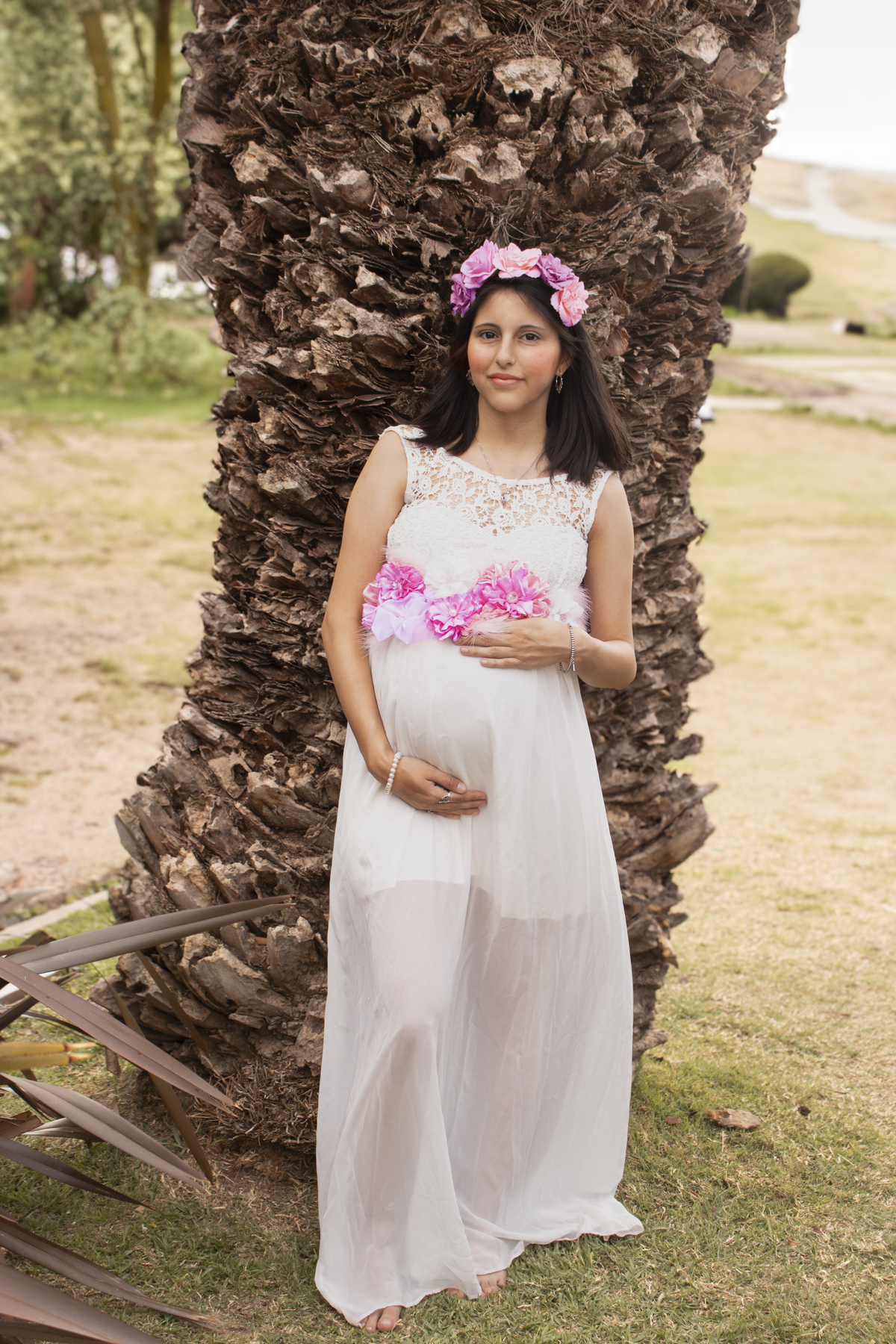 embarazada plano general apoyada en tronco de palmera, fondo de plantas