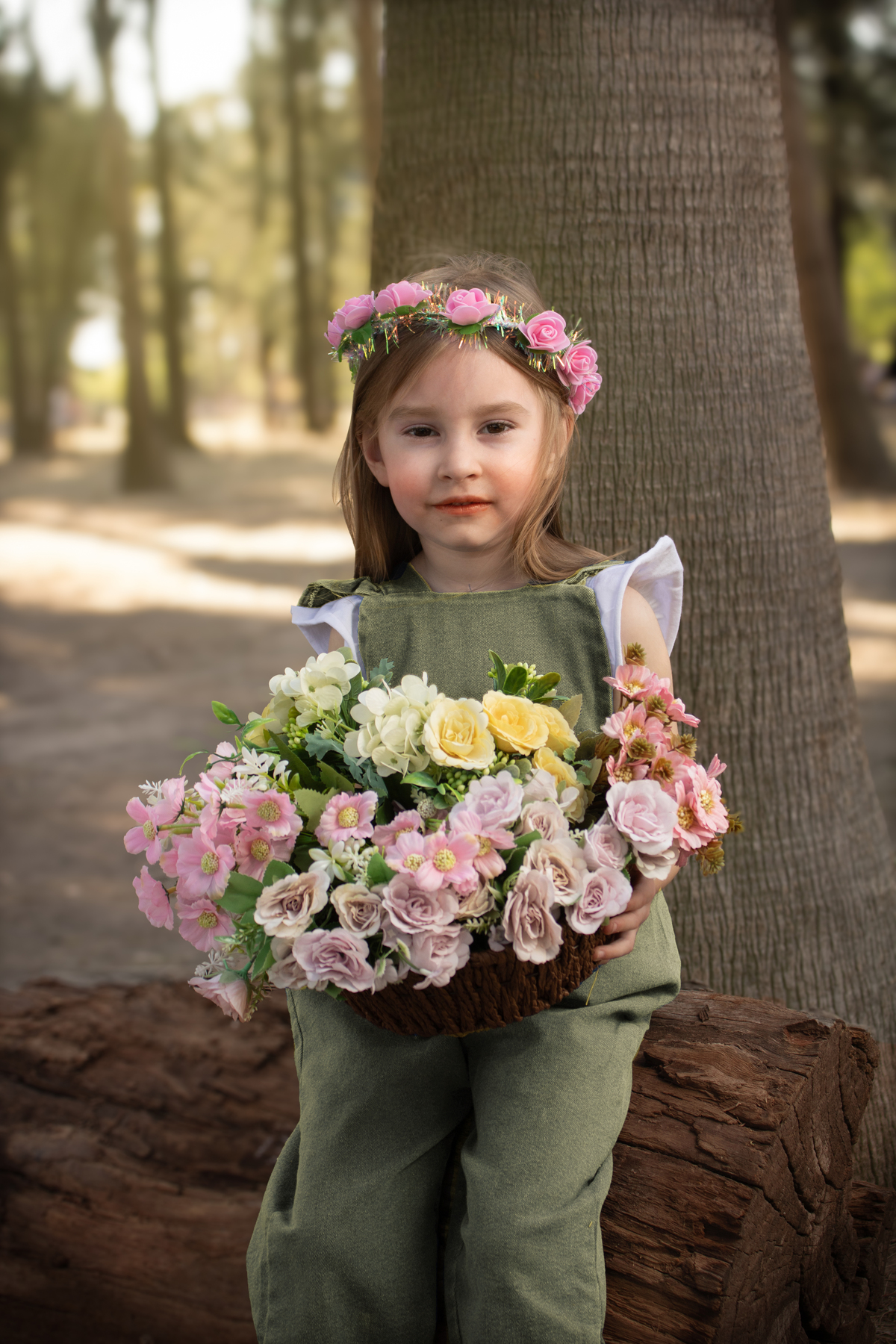 Niña sentada sobre un tronco con un cesto con flores en el bosque