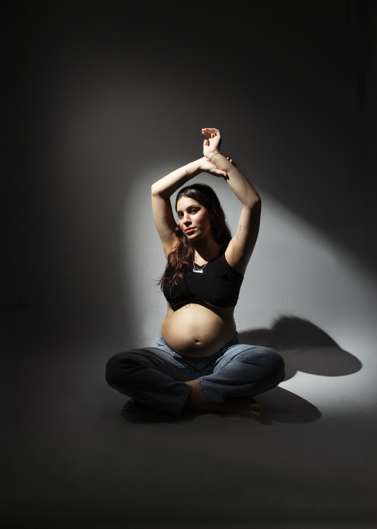 embarazada con ropa informal sentada sobre el piso , fotografía con fondo circular iluminado