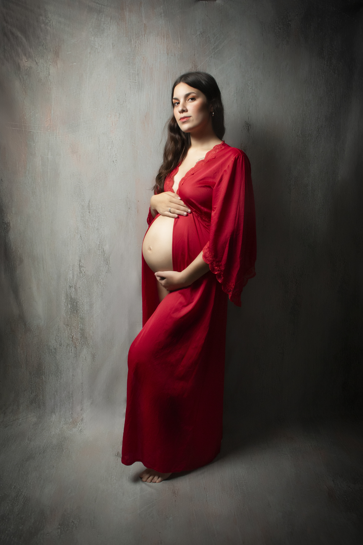embarazada de perfil mostrando la panza con una bata roja