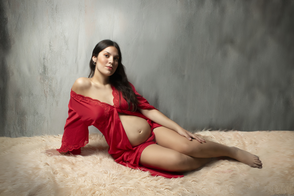 embarazada  con bata roja recostada sobre una alfombra