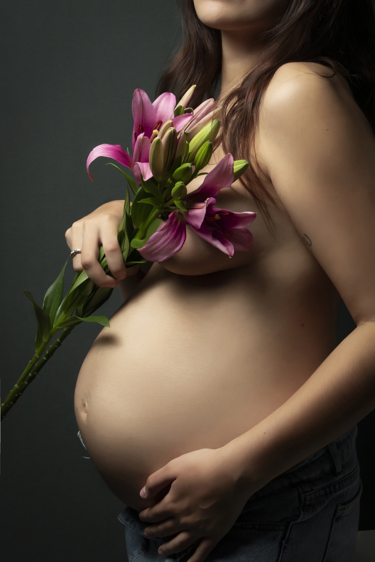 embarazada con el torso desnudo cubriéndose con flores de lilium, primer plano cuerpo 