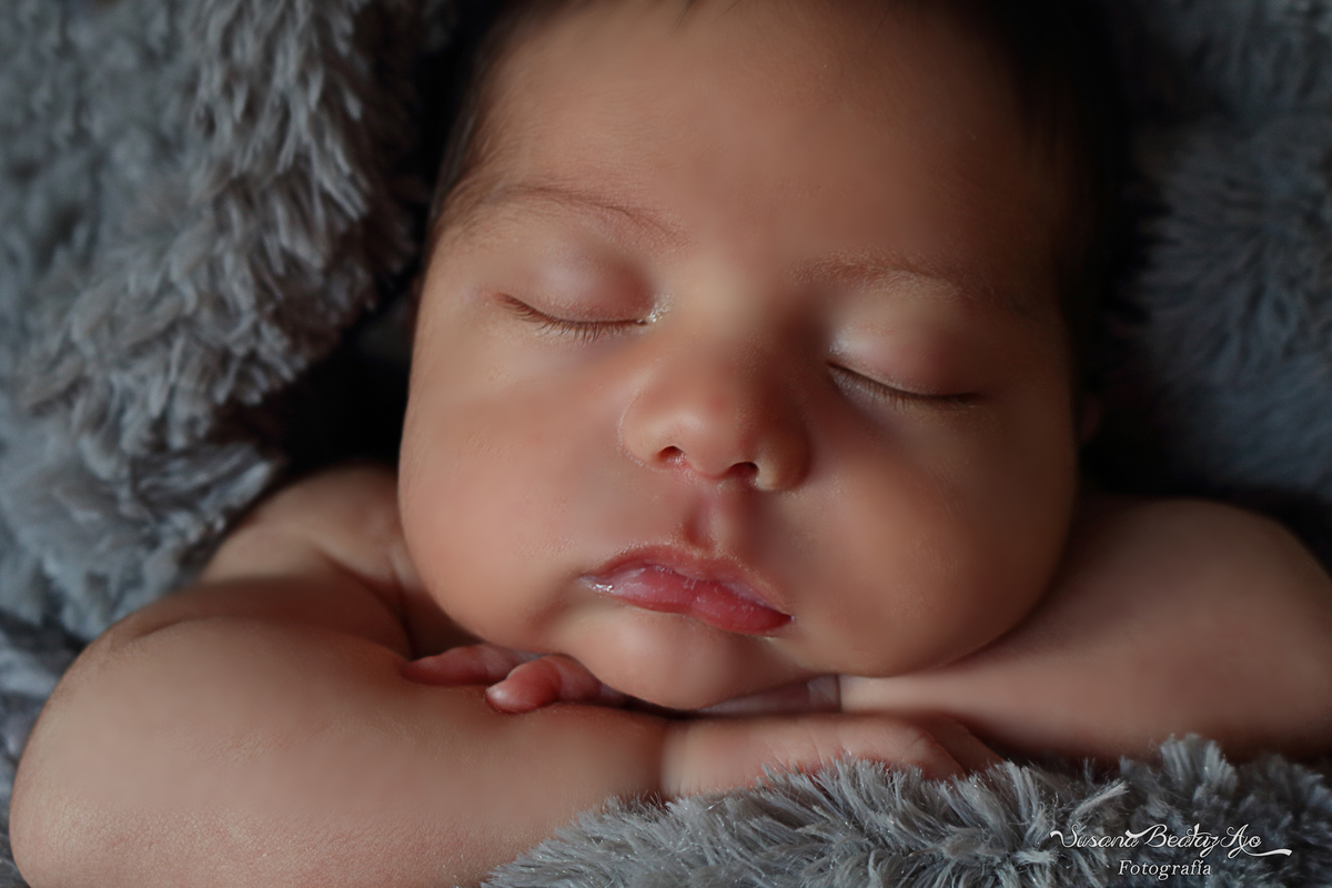 cara de bebe de frente apoyado cobre los brazos, envuelto en piel sintética gris