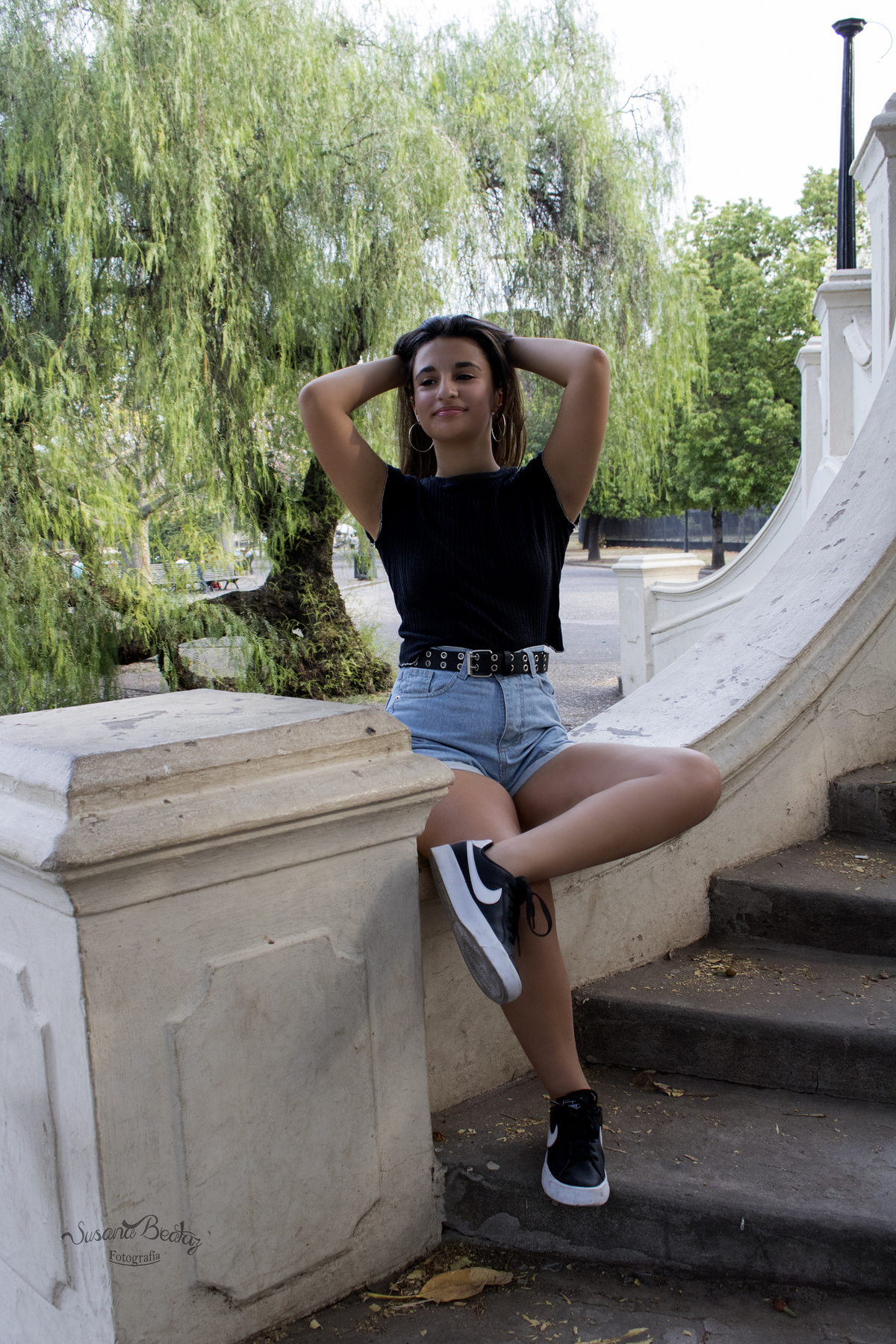 plano general quinceañera sentada sobre baranda de escalera, levantándose el pelo