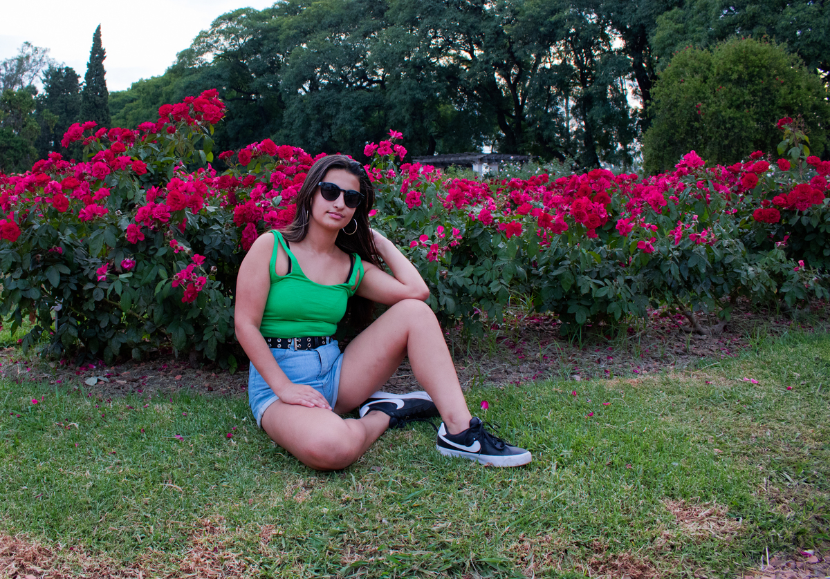 quinceañera con lentes de sol, sentada delante del rosedal