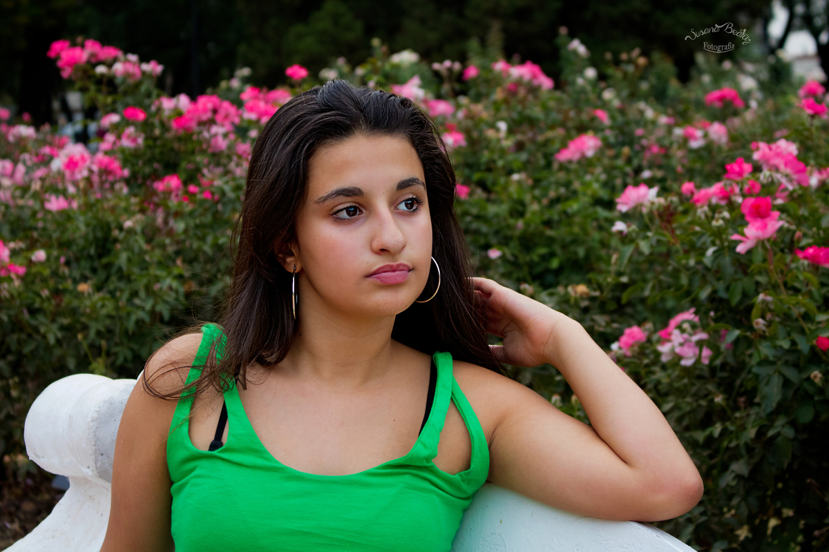 retrato quinceañera sentada en banco delante de un rosedal