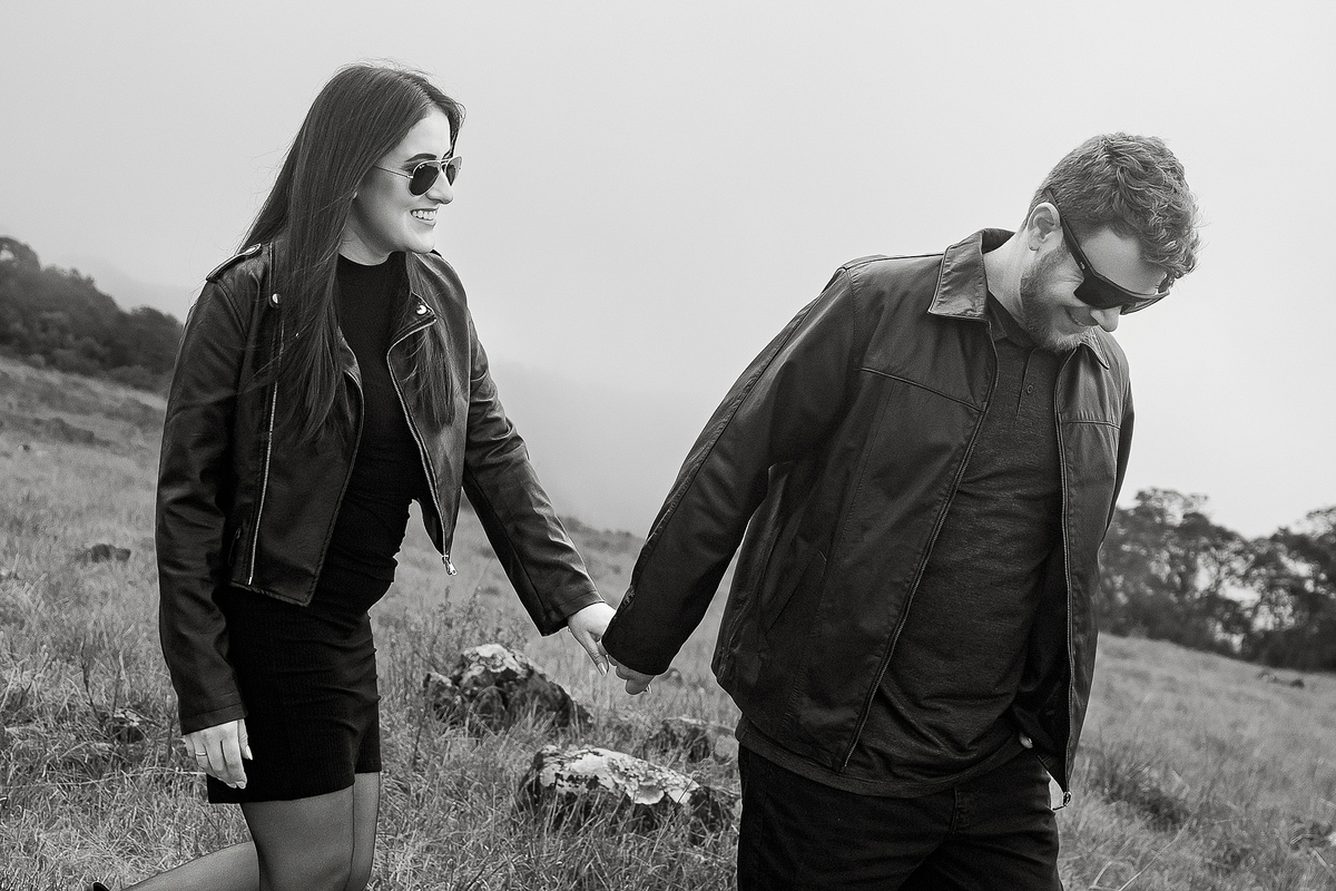 Casal caminhando de mãos dadas na serra com clima nublado.