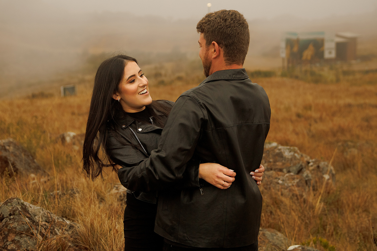 Casal abraçado em campo dourado durante o pôr do sol.