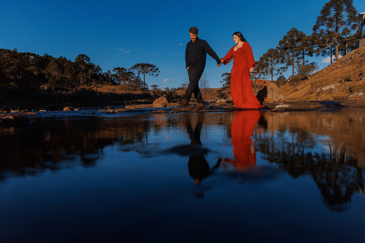 Casal refletido na água ao pôr do sol com vestido vermelho.
Foto cinematográfica de ensaio pré-casamento na Serra do Rio do Rastro.