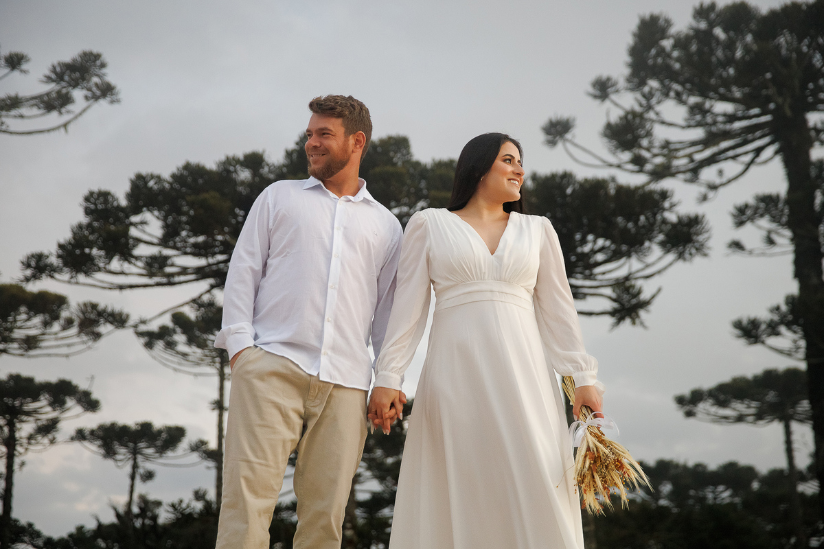 Casal de branco caminhando em campo aberto.
Imagem clean e elegante de ensaio pré-casamento em Bom Jardim da Serra.