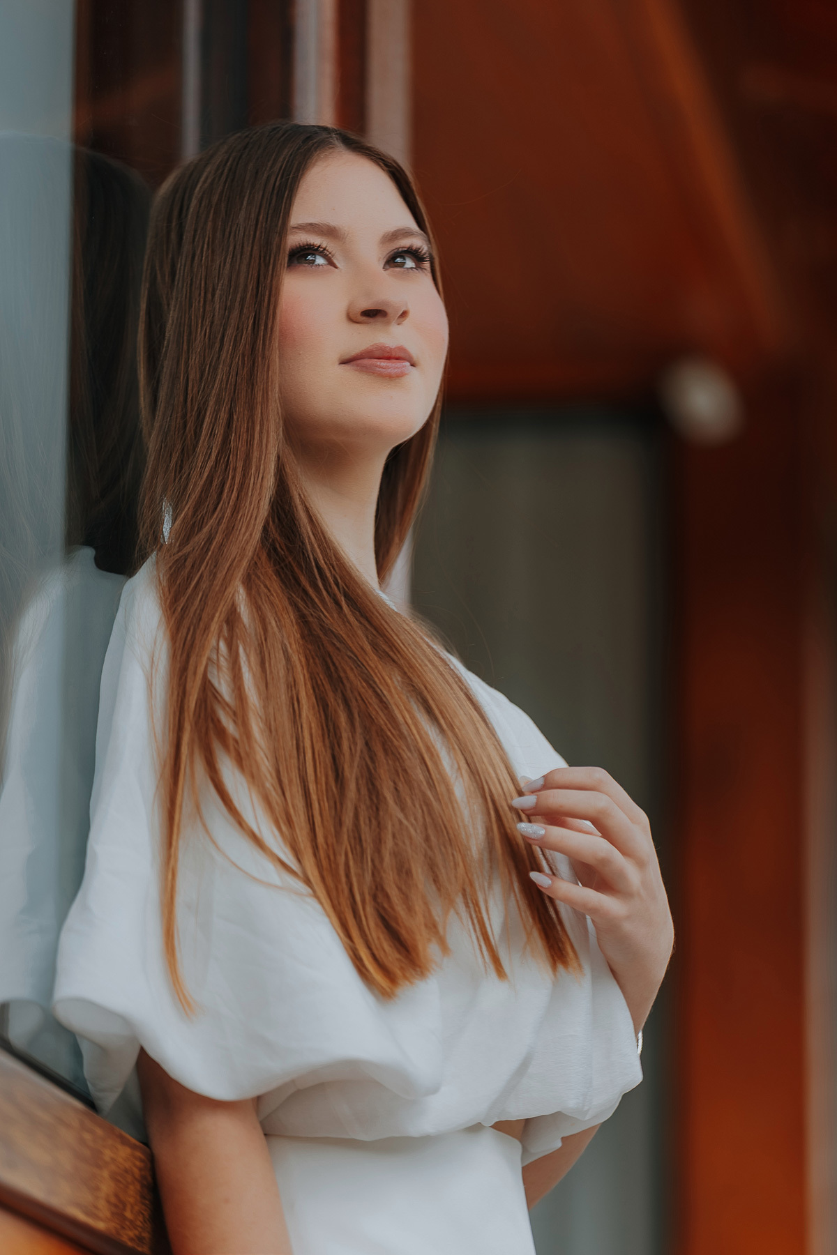 Laís posa em um momento de introspecção na varanda de madeira da Fazenda Favorita. A luz suave realça a naturalidade e o encanto típico dos ensaios de 15 anos no campo.
