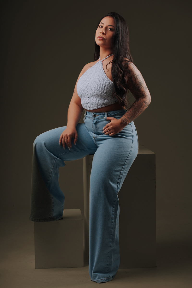 Pose sentada em jeans com fundo neutro
Foto elegante e moderna do ensaio de 26 anos, mostrando postura e atitude em ambiente de estúdio profissional.