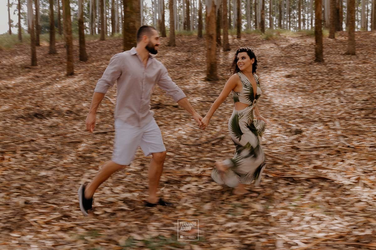 casal correndo entre os eucaliptos no ensaio de casal pre casamento