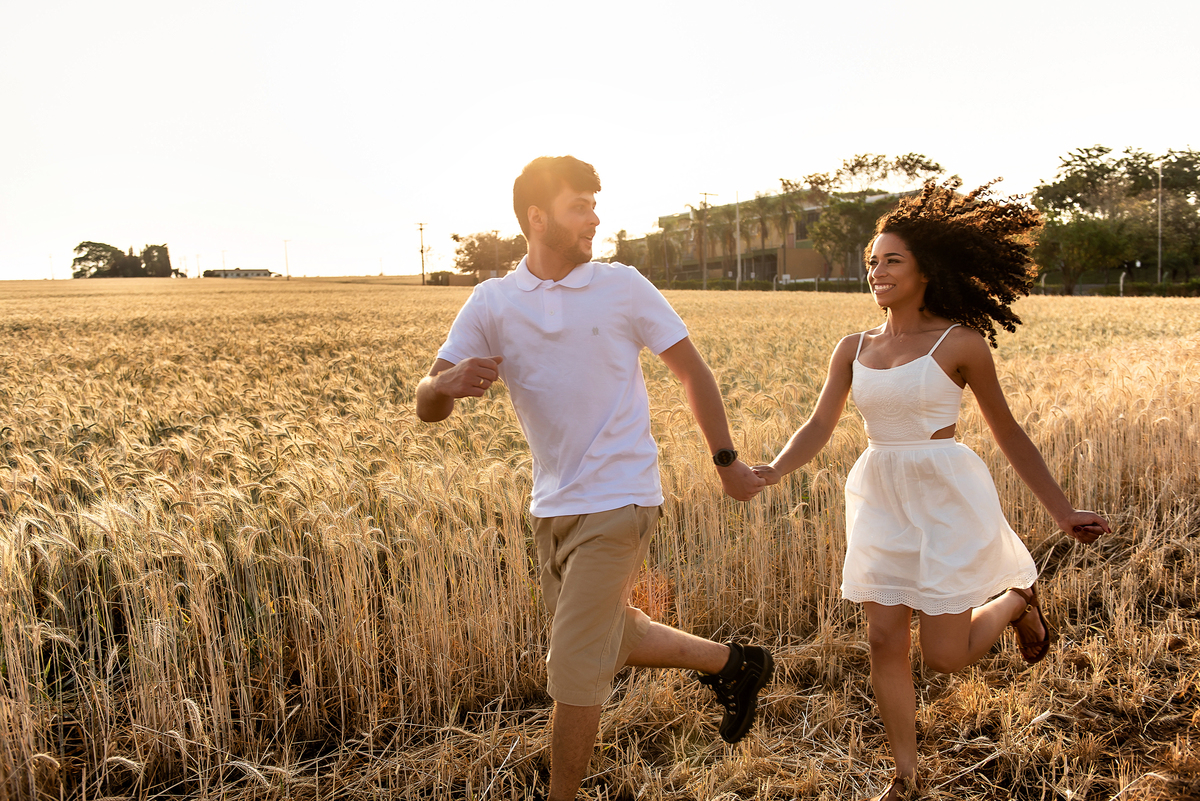 casal correndo em campo de trigo com o por do sol ao fundo em Holambra