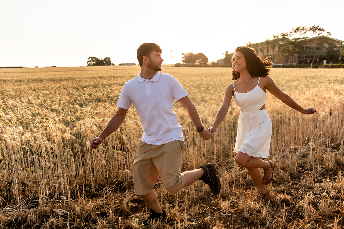 casal correndo em campo de trigo com o por do sol ao fundo em Holambra