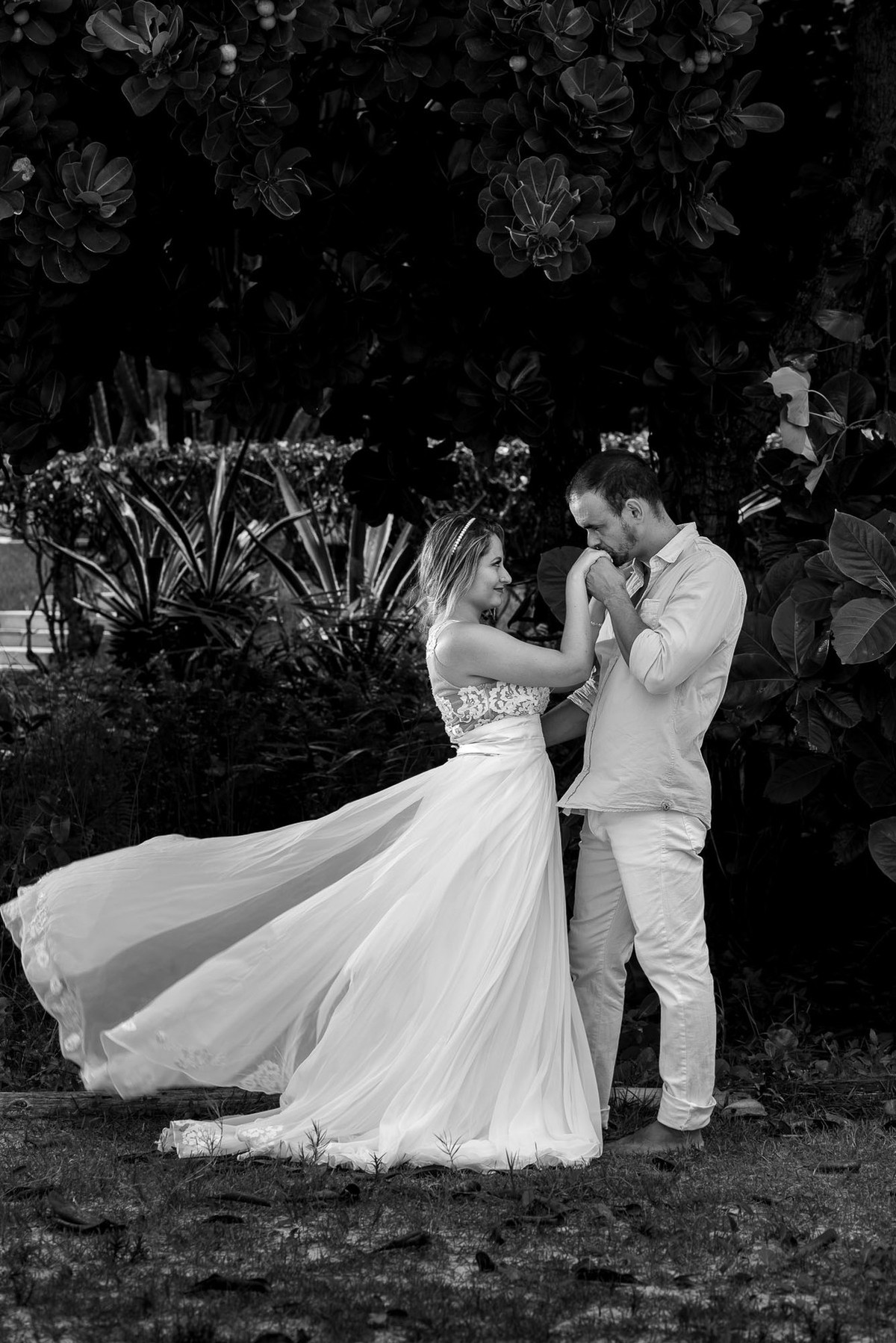 noivo beija mão da noiva com vestindo voando com o vento na praia do sao pedro no guaruja