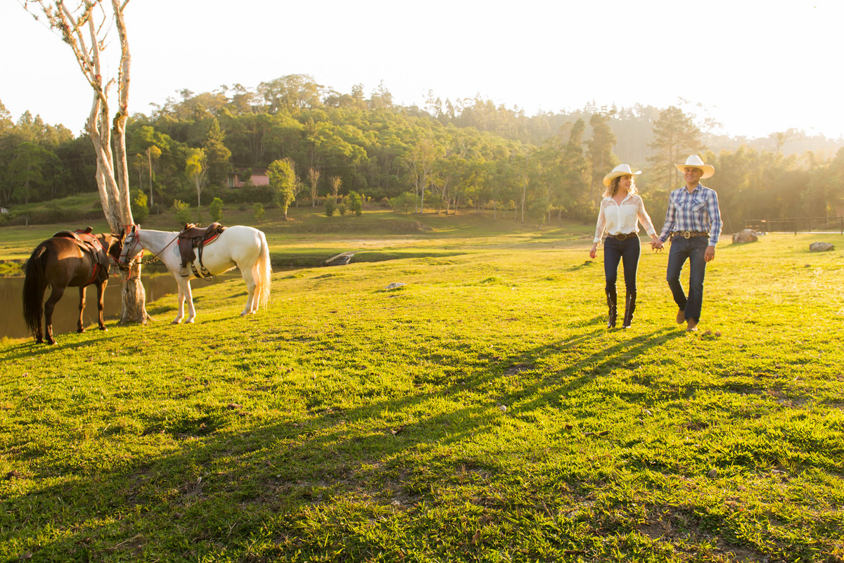 casal caminhando com a luz do por do sol e cavalos amarrados ao lado em sitio na cidade de Juquitiba