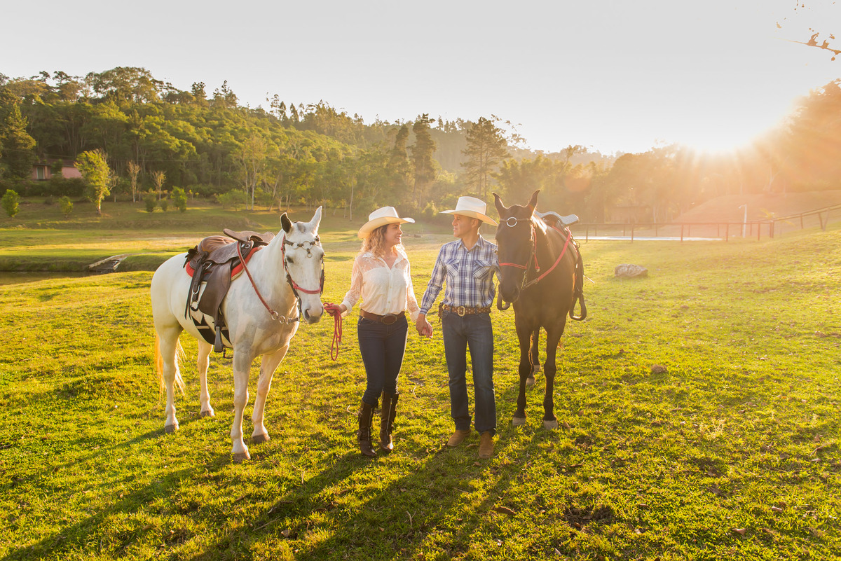 casal caminhando segurando as redes do cavalo com a luz do por do sol em sitio na cidade de Juquitiba