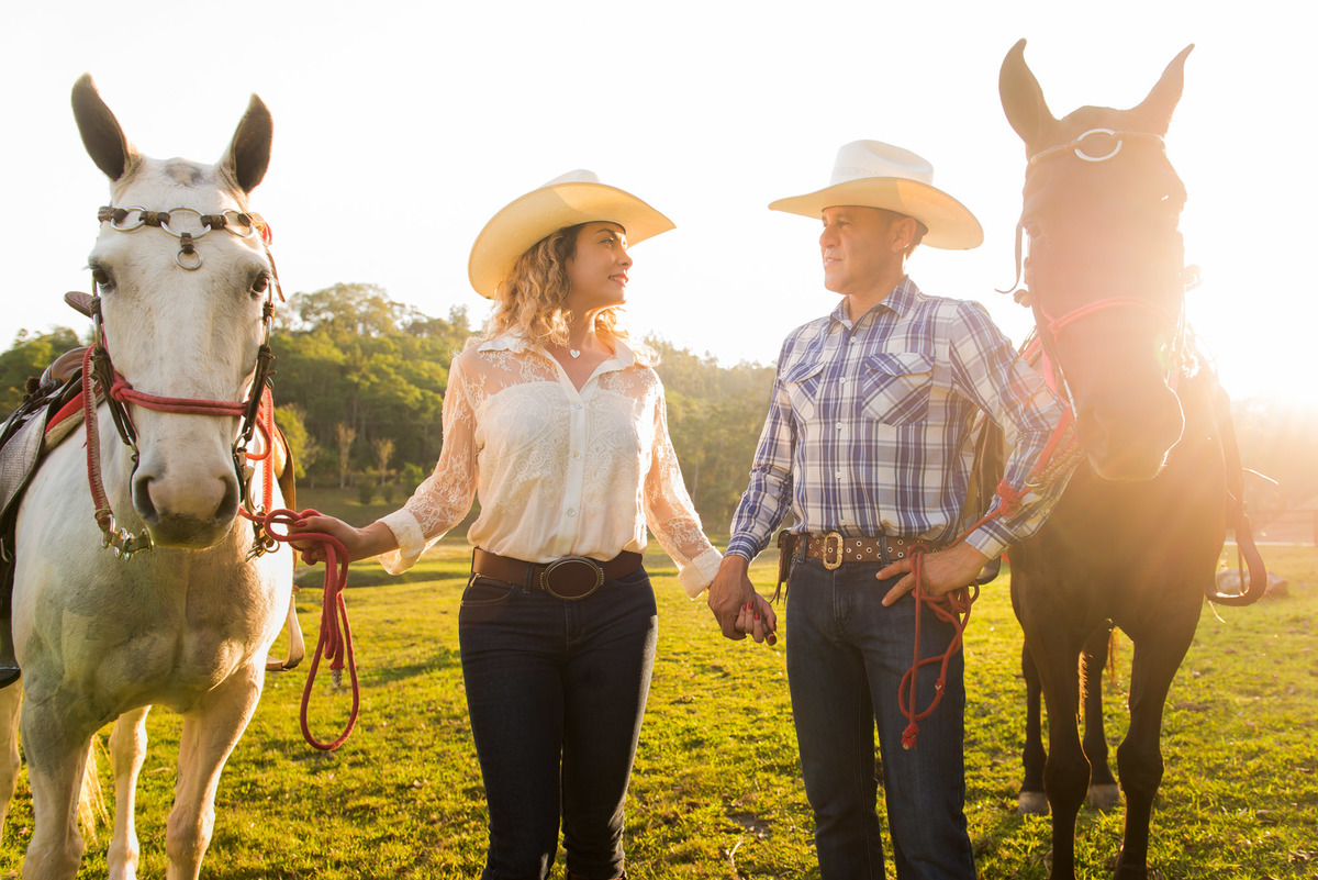 casal caminhando segurando as redes do cavalo com a luz do por do sol em sitio na cidade de Juquitiba