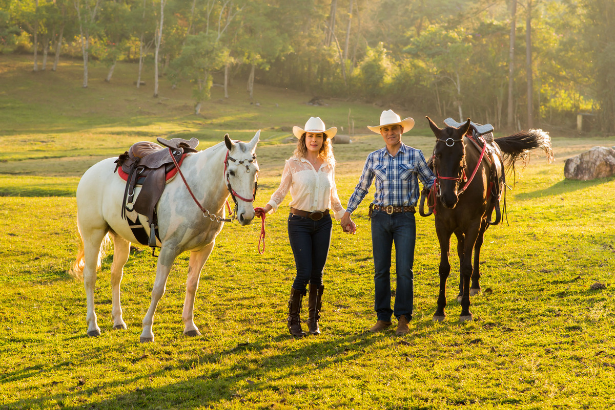 casal caminhando segurando as redes do cavalo com a luz do por do sol em sitio na cidade de Juquitiba