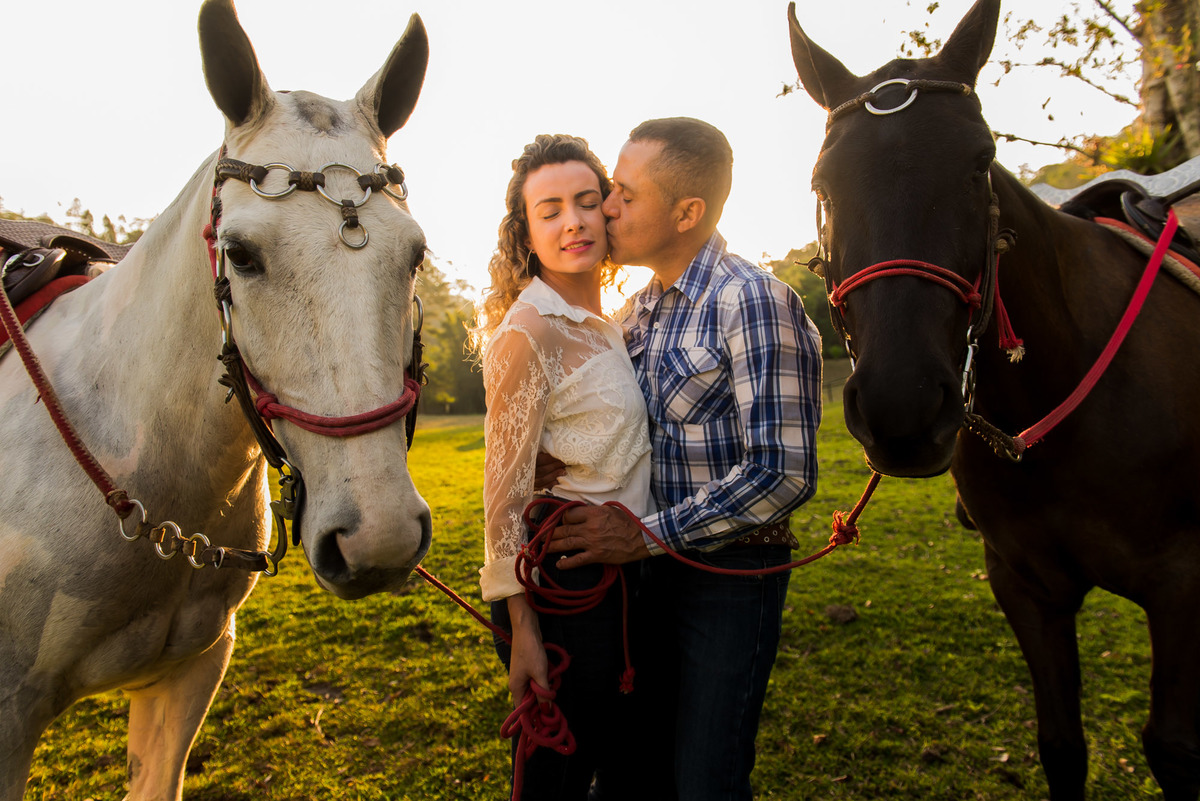casal se beijando segurando as redes do cavalo com a luz do por do sol em sitio na cidade de Juquitiba