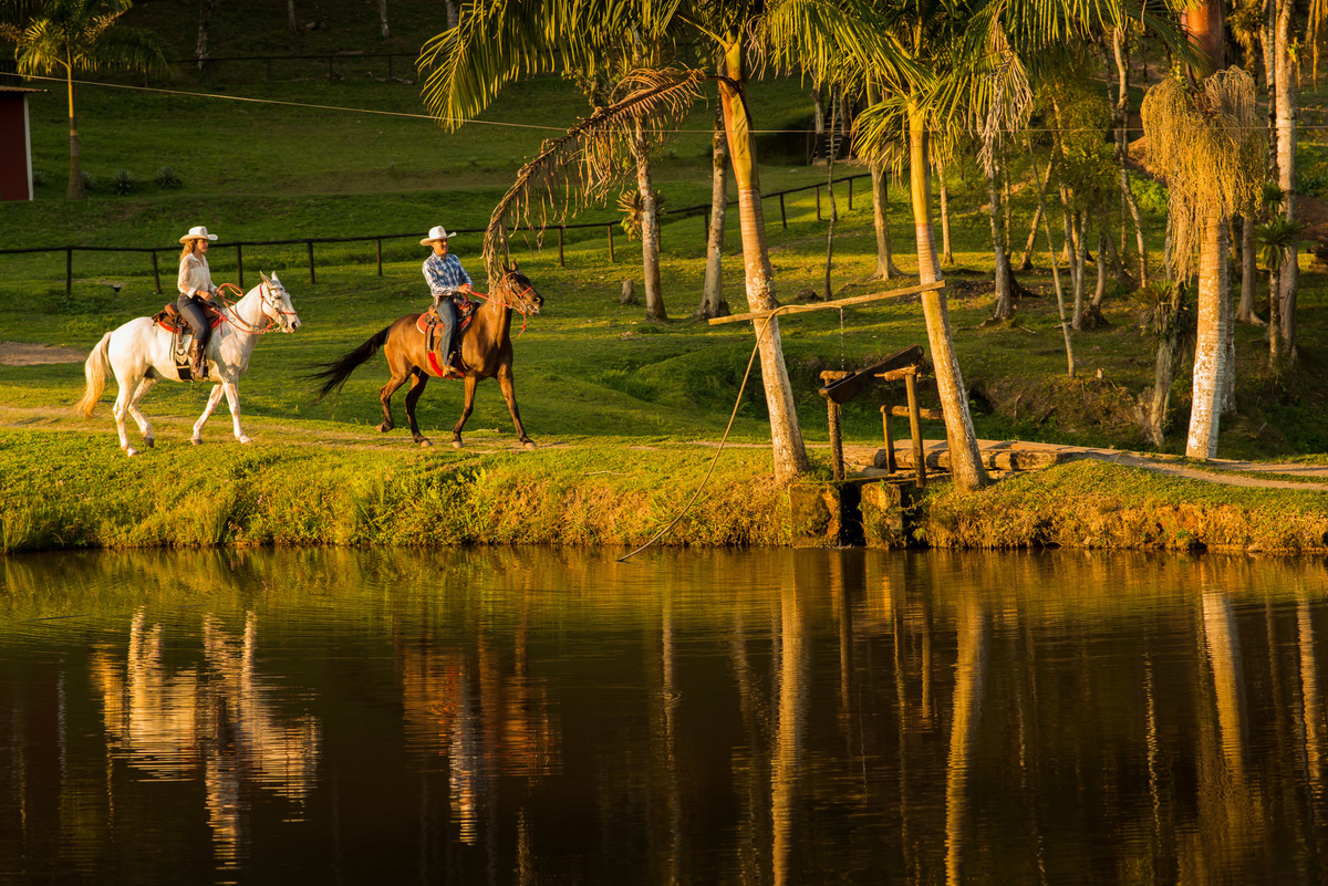 casal cavalgando na beira do lago com a luz do por do sol em sitio na cidade de Juquitiba