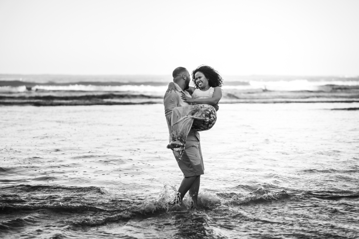 noivo segurando noiva no colo na praia do Iporanga no Guarujá com por do sol ao fundo