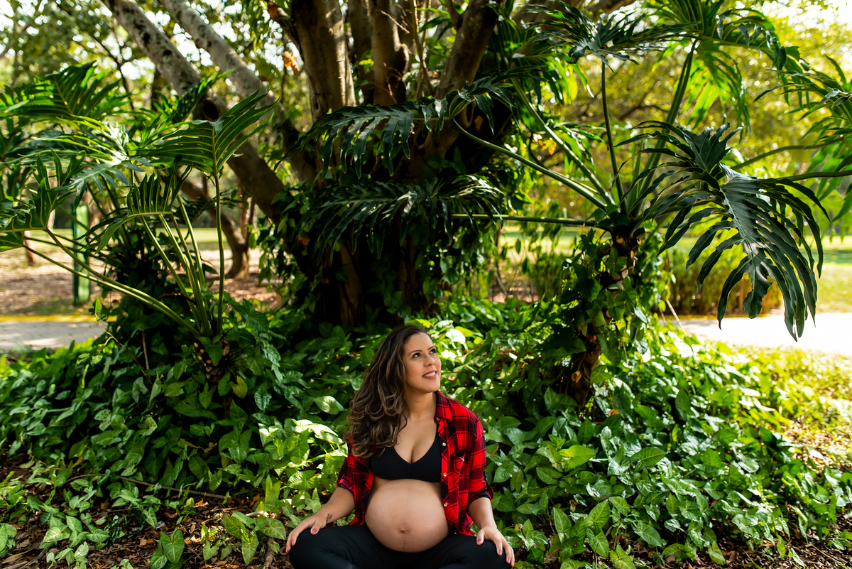 ensaio de gestante com mulher sentada no chão com folhas verdes ao redor no parque villa lobos em São Paulo