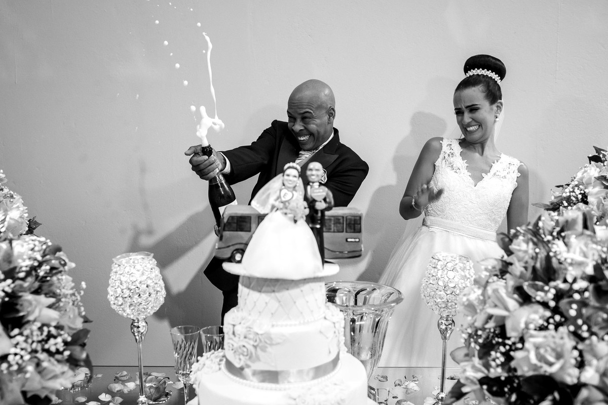 noivo estourando a garrafa de champagnhe com noiva se assustando na mesa do bolo buffet Reis Recepções