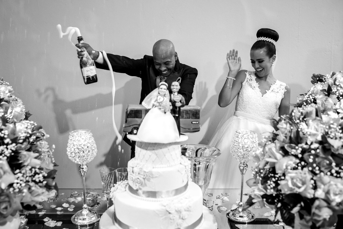 noivo estourando a garrafa de champagnhe com noiva se assustando na mesa do bolo buffet Reis Recepções