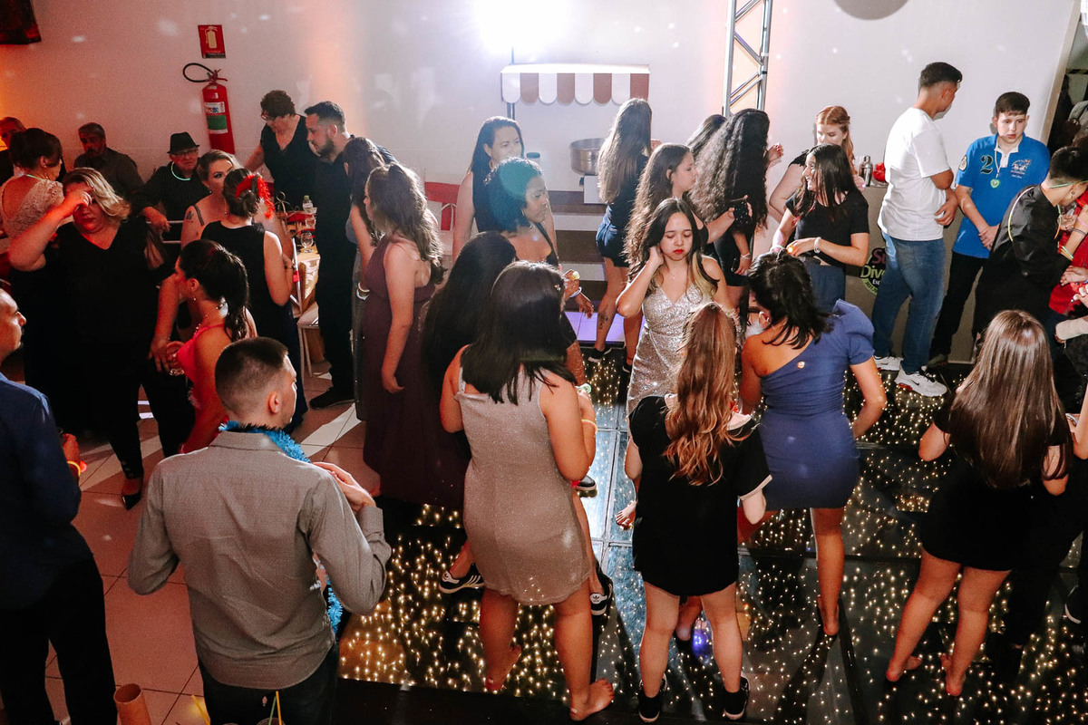 Luiza apresentando coreografia animada com amigas na festa de 15 anos, usando vestido dourado curto e coroa.