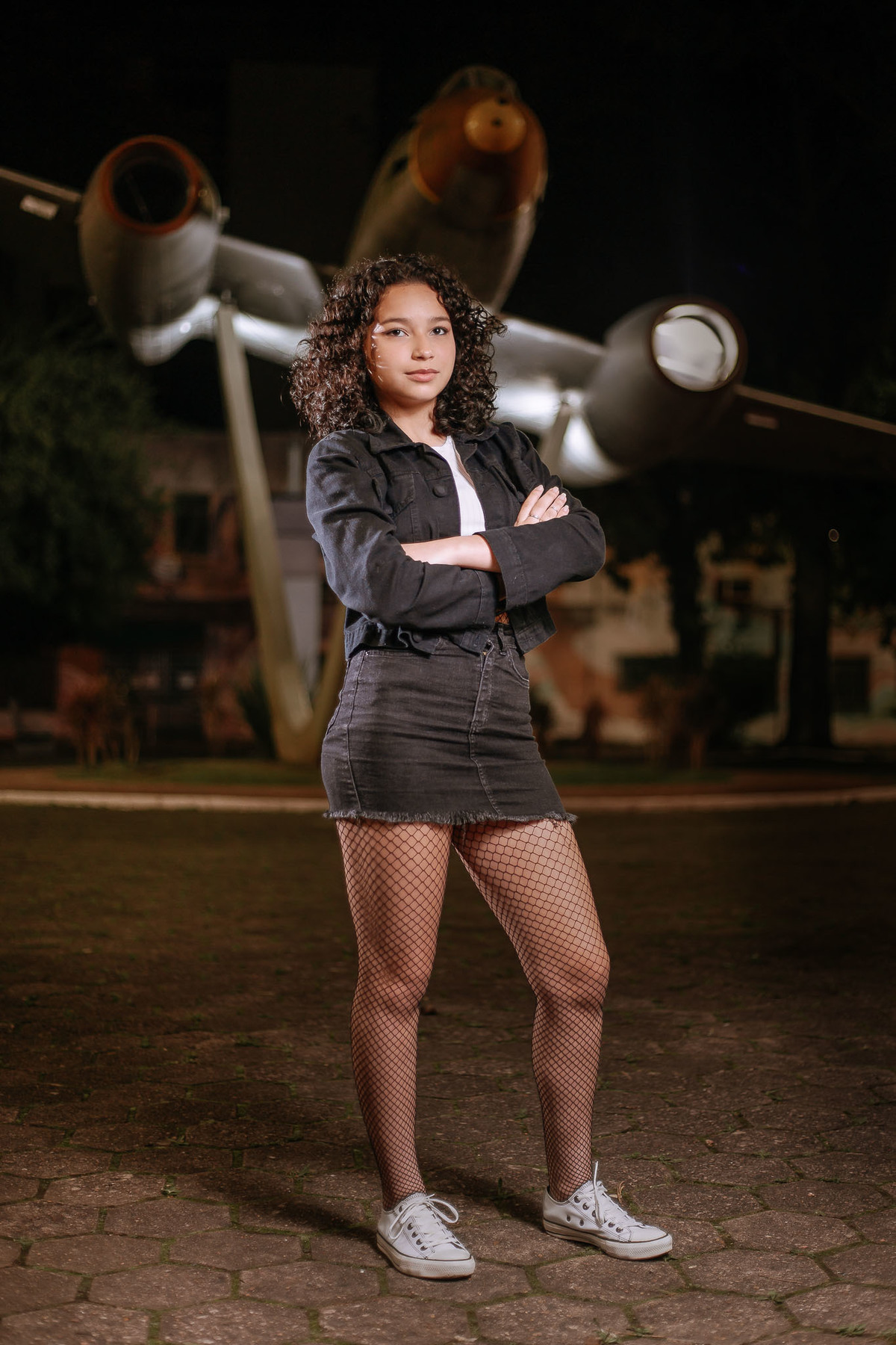 Ensaio de 15 anos em Canoas com estilo urbano noturno, debutante em frente a avião com iluminação dramática