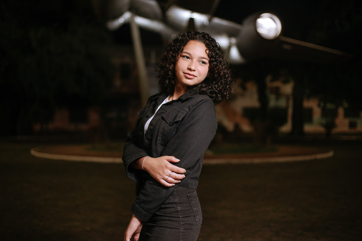 Ensaio de 15 anos em Canoas com estilo urbano noturno, debutante em frente a avião com iluminação dramática