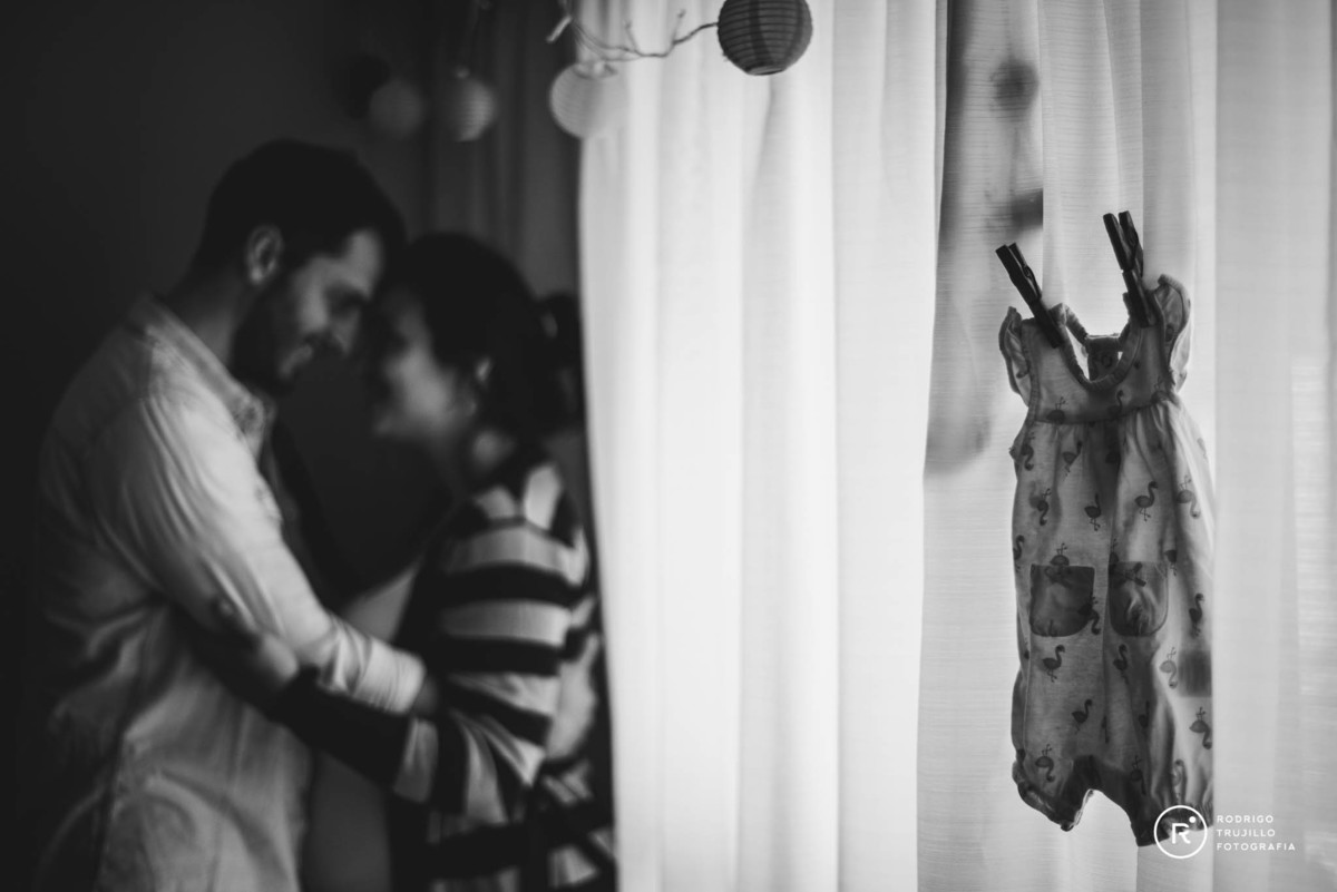 los papás de amelia estan en fondo de la habitacion, sobre la cortina del living cuelga un vestido de amelia, futuros papás felices, rodrigo trujillo fotografia