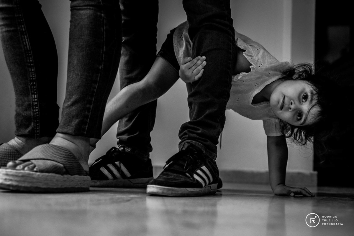 niña abrazando la pierna del padre en la sesion de fotos de la panza de su mama retratando a su hermanita.
