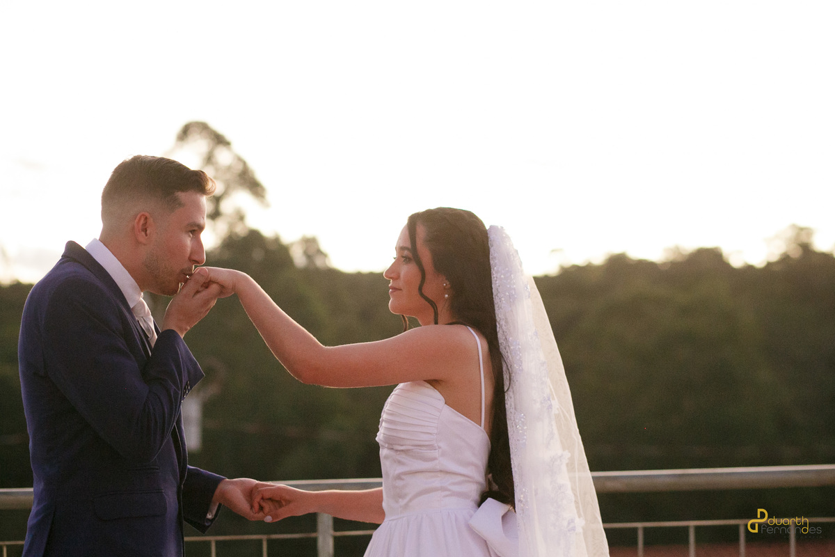 Noivo Lucas beijando a mão da noiva Mariana, pôr do sol, momento romântico do casamento em Veredinha MG