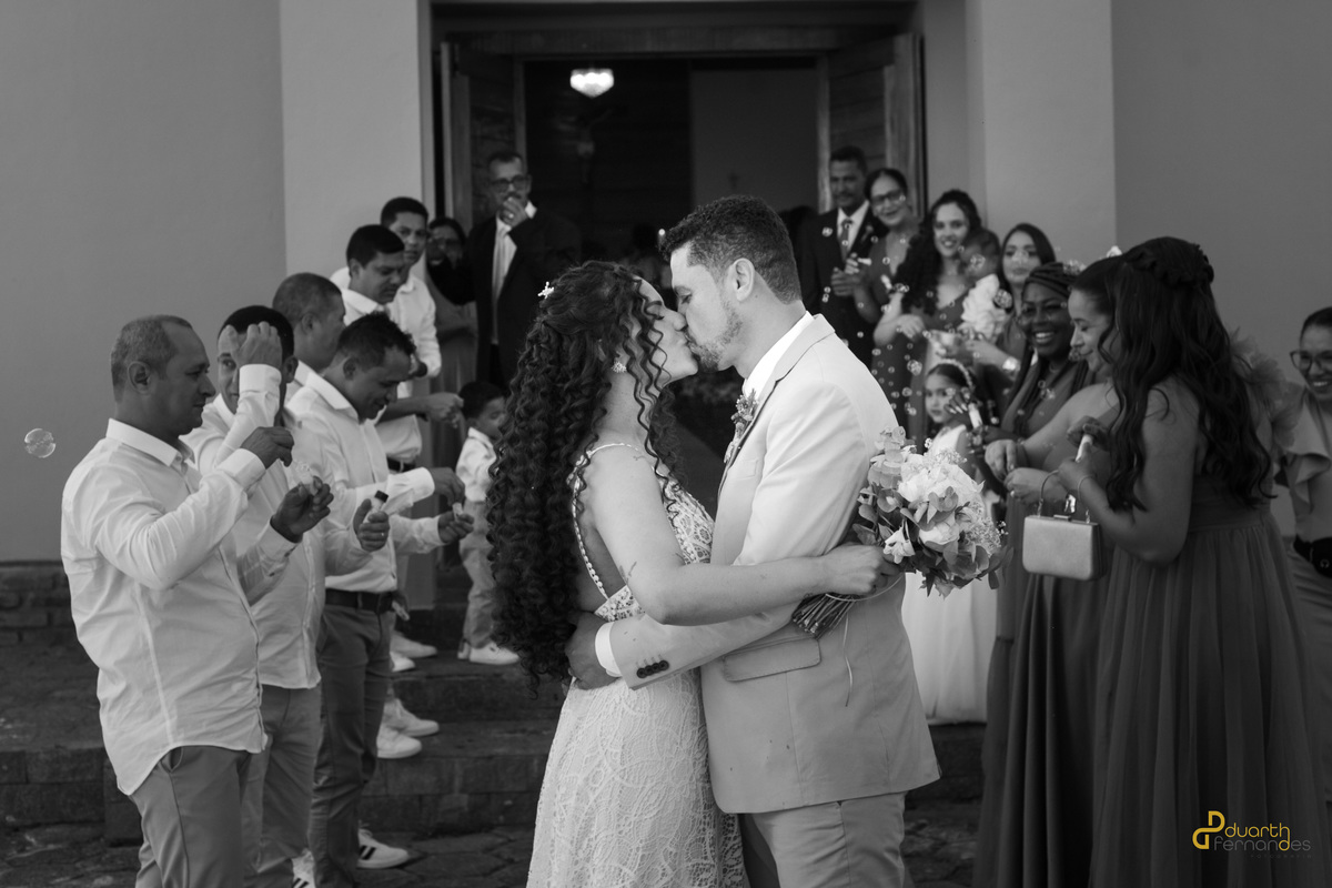 Leandro e Jacyara na cerimônia de casamento, trocando olhares e segurando as alianças. Momento emocionante da união, com a atenção dos convidados em fundo difuso e uma atmosfera de celebração.