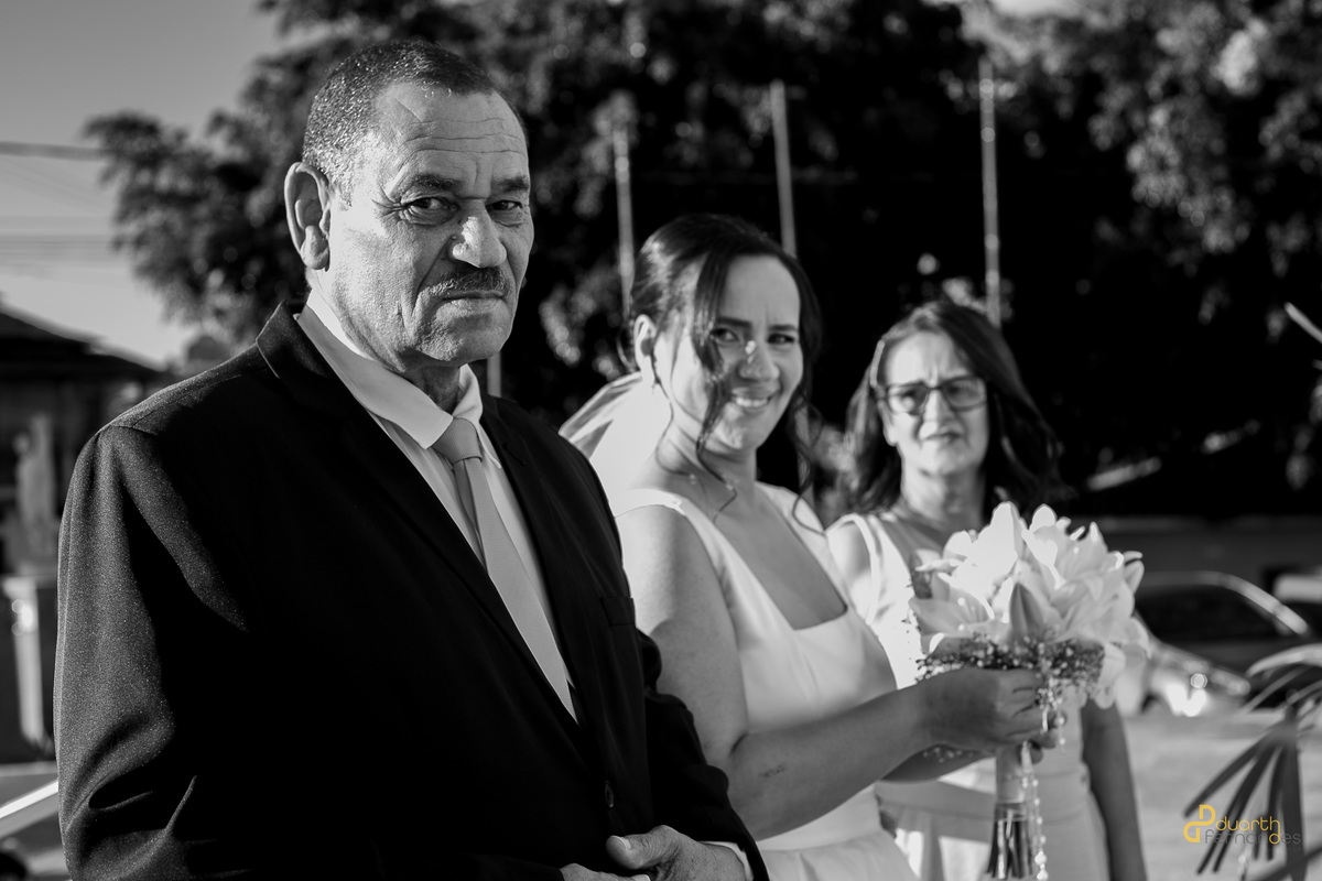 Retrato emocionante em preto e branco da noiva com seu pai antes de entrar na igreja. O olhar marcante do pai do noivo e o sorriso da noiva no casamento em Itamarandiba.
