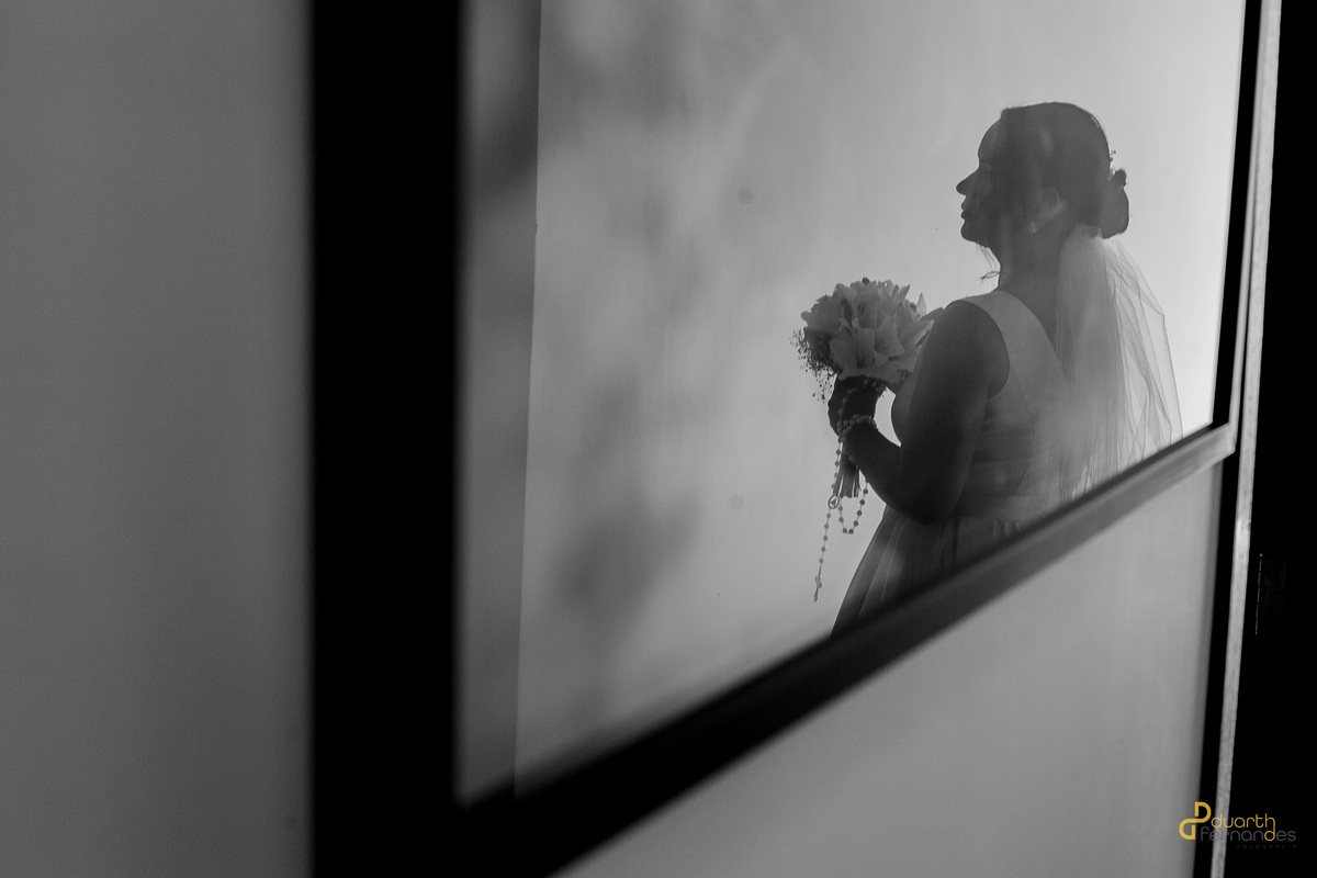 Retrato em preto e branco da noiva Nicolly em silhueta, com o véu e o buquê de lírios em destaque. Olhar contemplativo e cheio de emoção antes do casamento em Itamarandiba.