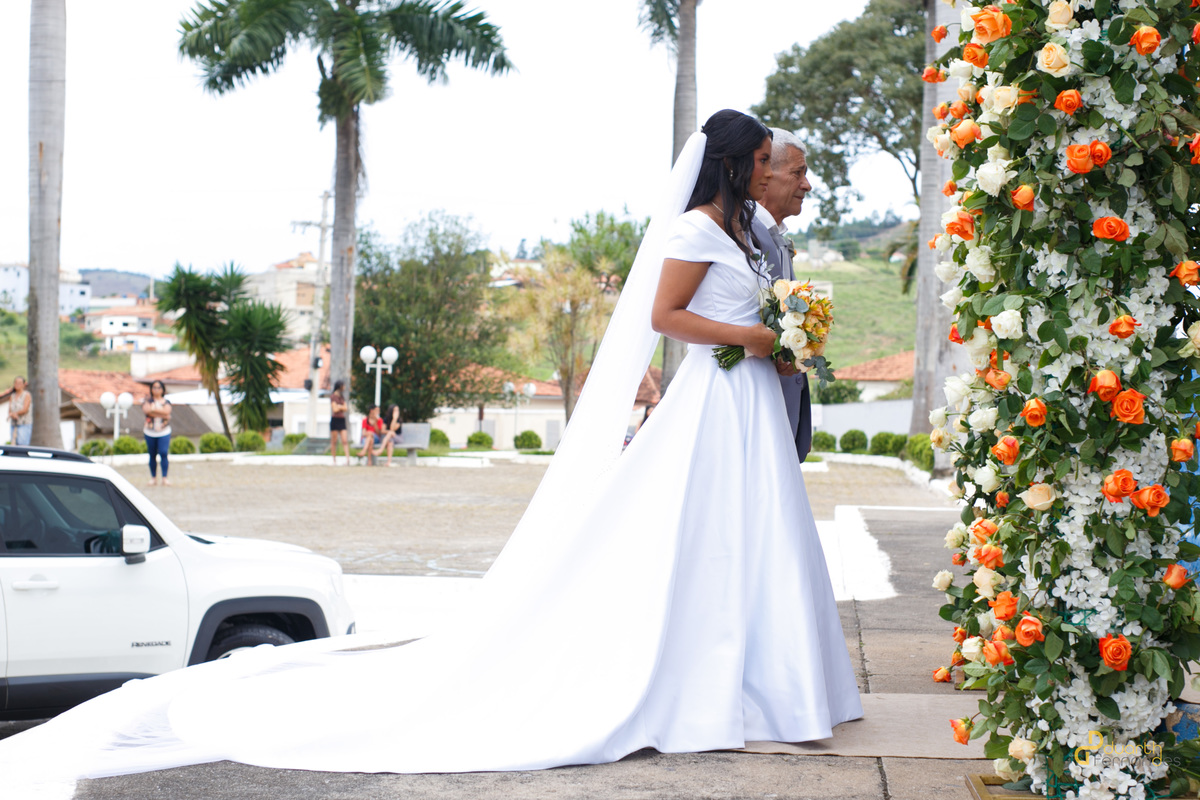 Ângulo contra-plongé da noiva Gardênia ajustando o vestido branco com palmeiras ao fundo, destacando a beleza da noiva. Fotografia de casamento em Aricanduva.