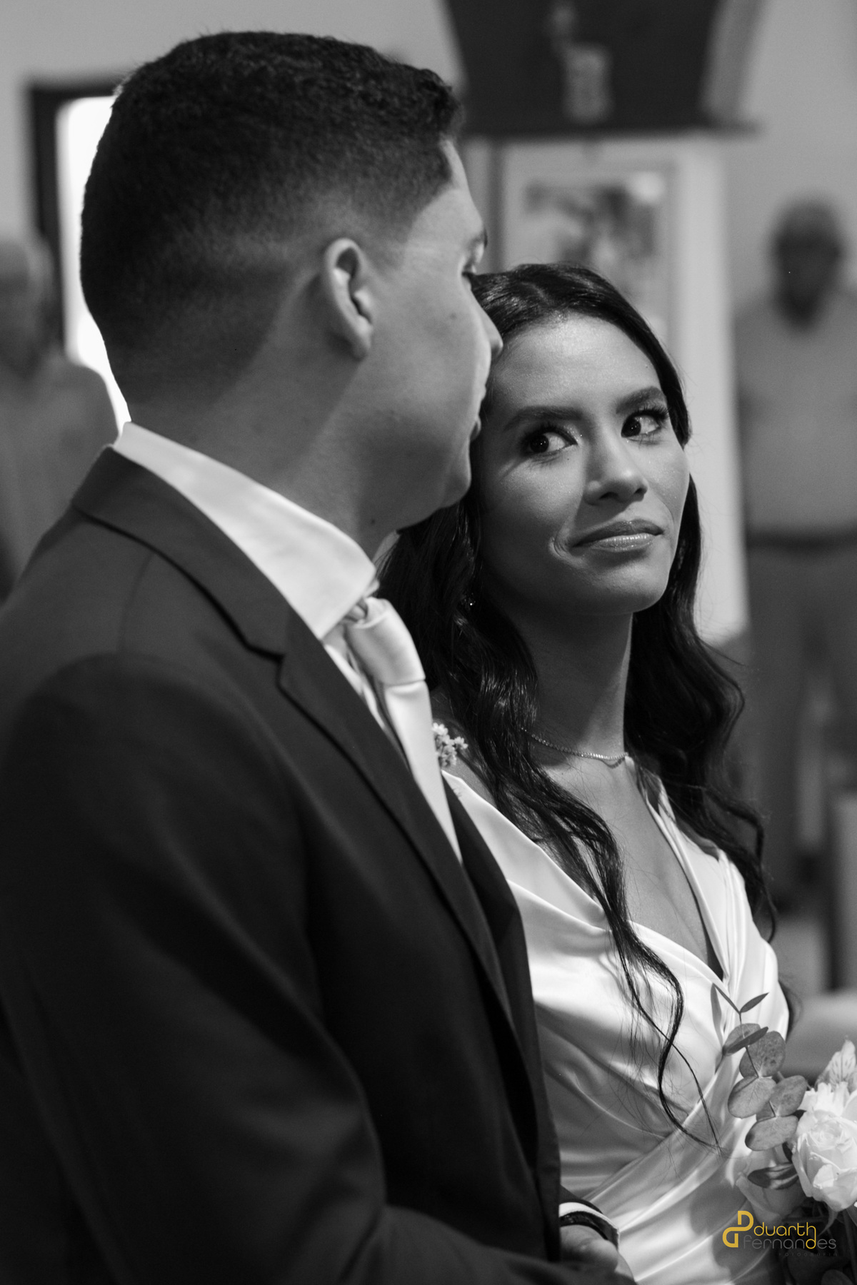 Foto em preto e branco com foco na noiva Gardênia olhando com admiração para o noivo Arthur durante a cerimônia religiosa. Registro expressivo de casamento em Aricanduva.