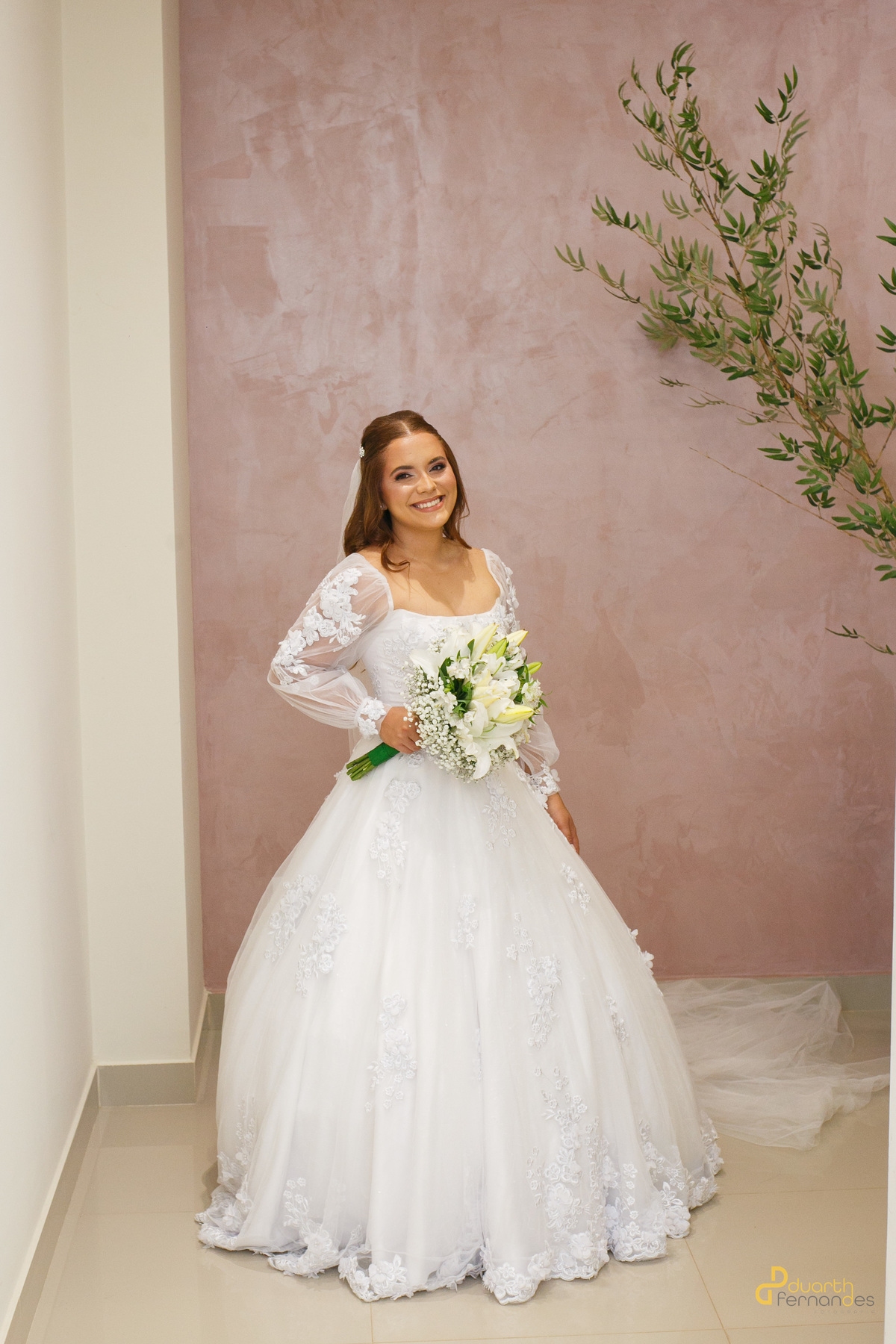 Retrato de plano inteiro da noiva Elen sorrindo com seu vestido de noiva clássico rodado e buquê de lírios brancos. Fotografia profissional por fotógrafo de casamento em Capelinha - MG.