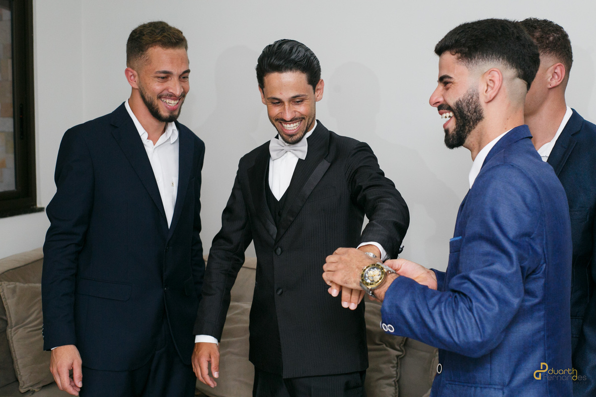 Noivo Dieique sorrindo e descontraído ao lado dos padrinhos de terno durante o making of em Capelinha - MG. Registro espontâneo feito por fotógrafo de casamento na região.