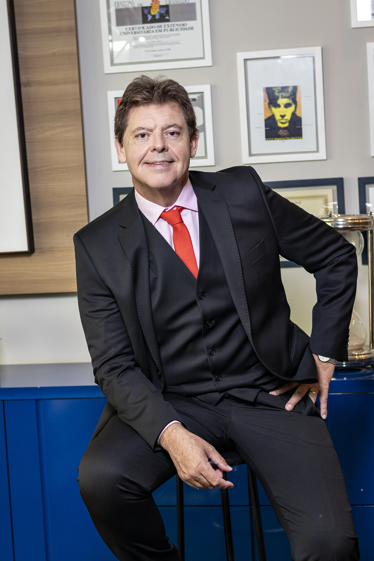 Em pé, apoiado em estante, de paletó preto.
